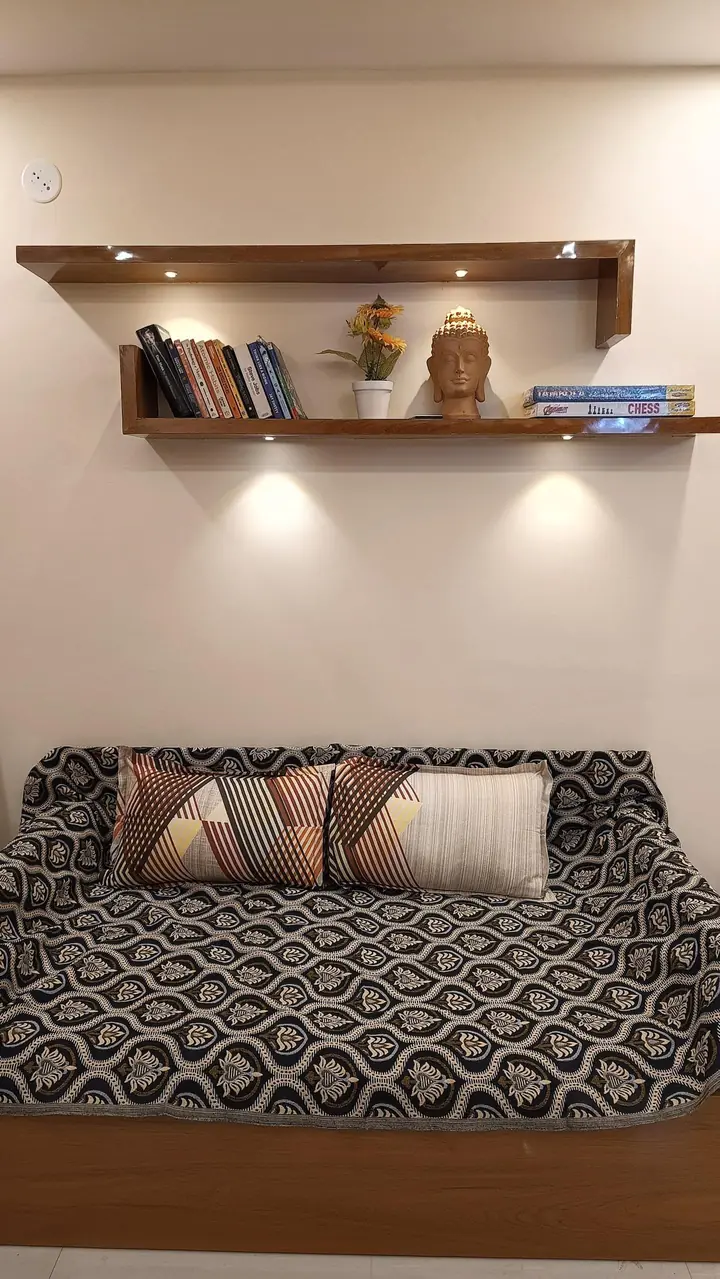 Sofa bed with patterned throw beneath a lit bookshelf